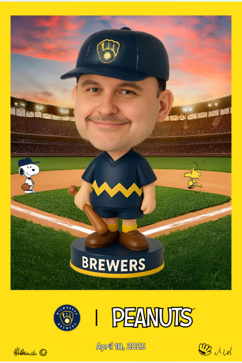 A bobblehead with a mans face, wearing a Brewers-themed Charlie Brown uniform, stands on a baseball field with Snoopy and Woodstock. Peanuts and Brewers logos are present.